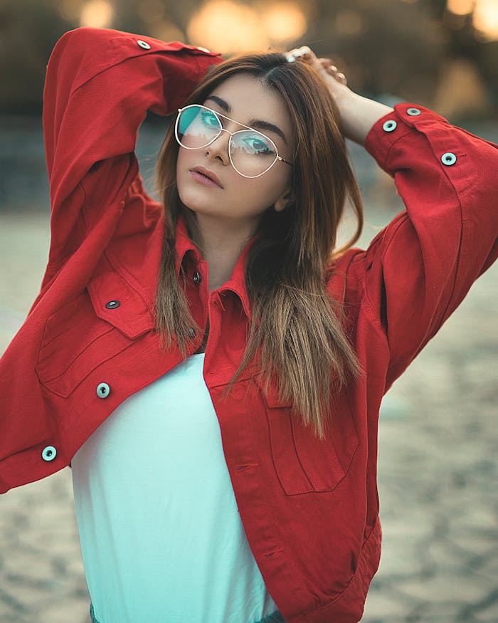 Services Stylish woman posing outdoors in a vibrant red jacket with eyeglasses.