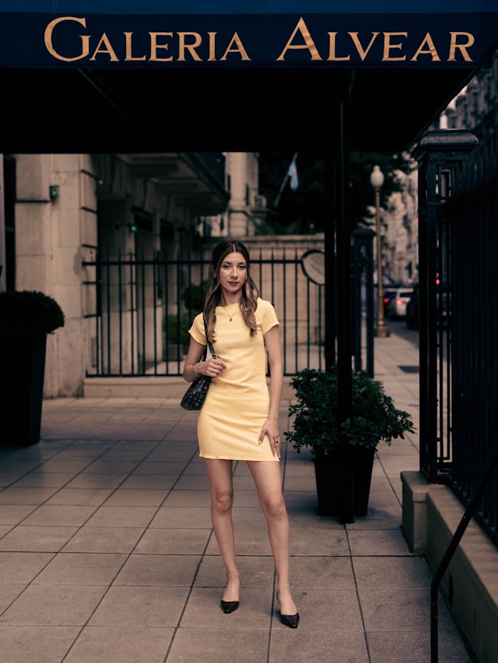 Services Fashionable woman in yellow dress standing outside Galeria Alvear on a city street.